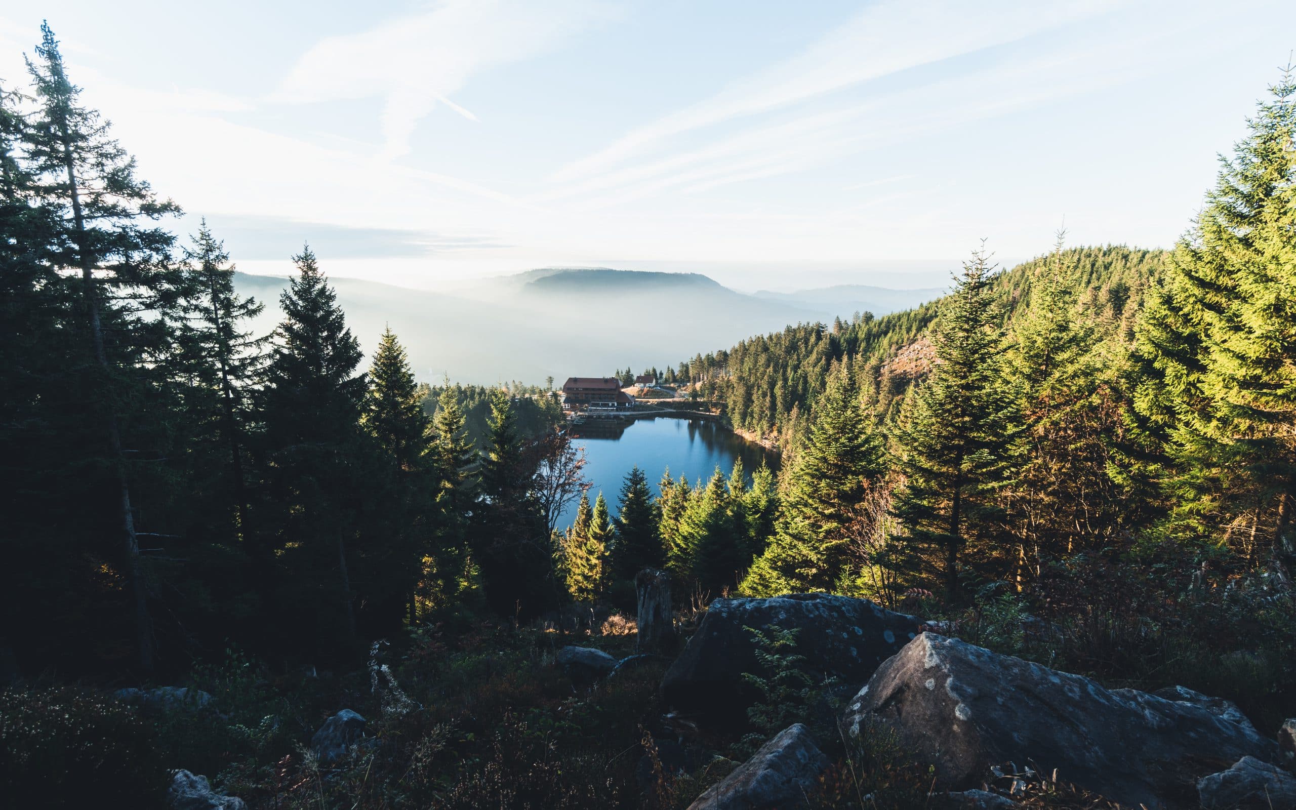 Bergsee mit Hotelanlage inmitten eines Tannenwaldes bei Morgenlicht – Symbolbild für Leisure-Destinationen im Sommer 2025